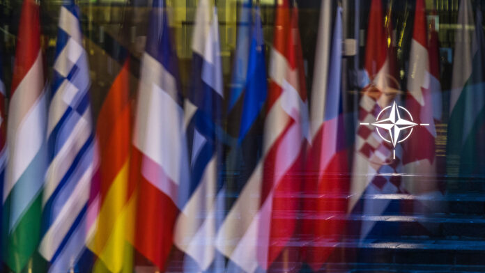 BRUSSELS, BELGIUM - APRIL 04: The NATO symbol is seen reflected in a window alongside the flags of some of the member countries before the start of the 75th anniversary celebrations on April 04, 2024 in Brussels, Belgium. The North Atlantic Treaty Organization (NATO) was founded 75 years ago in the wake of World War II and at the onset of the Cold War. Within the last year, it has added two new members, Finland and Sweden, who were spurred to seek membership following Russia's large-scale invasion of Ukraine. (Photo by Omar Havana/Getty Images)